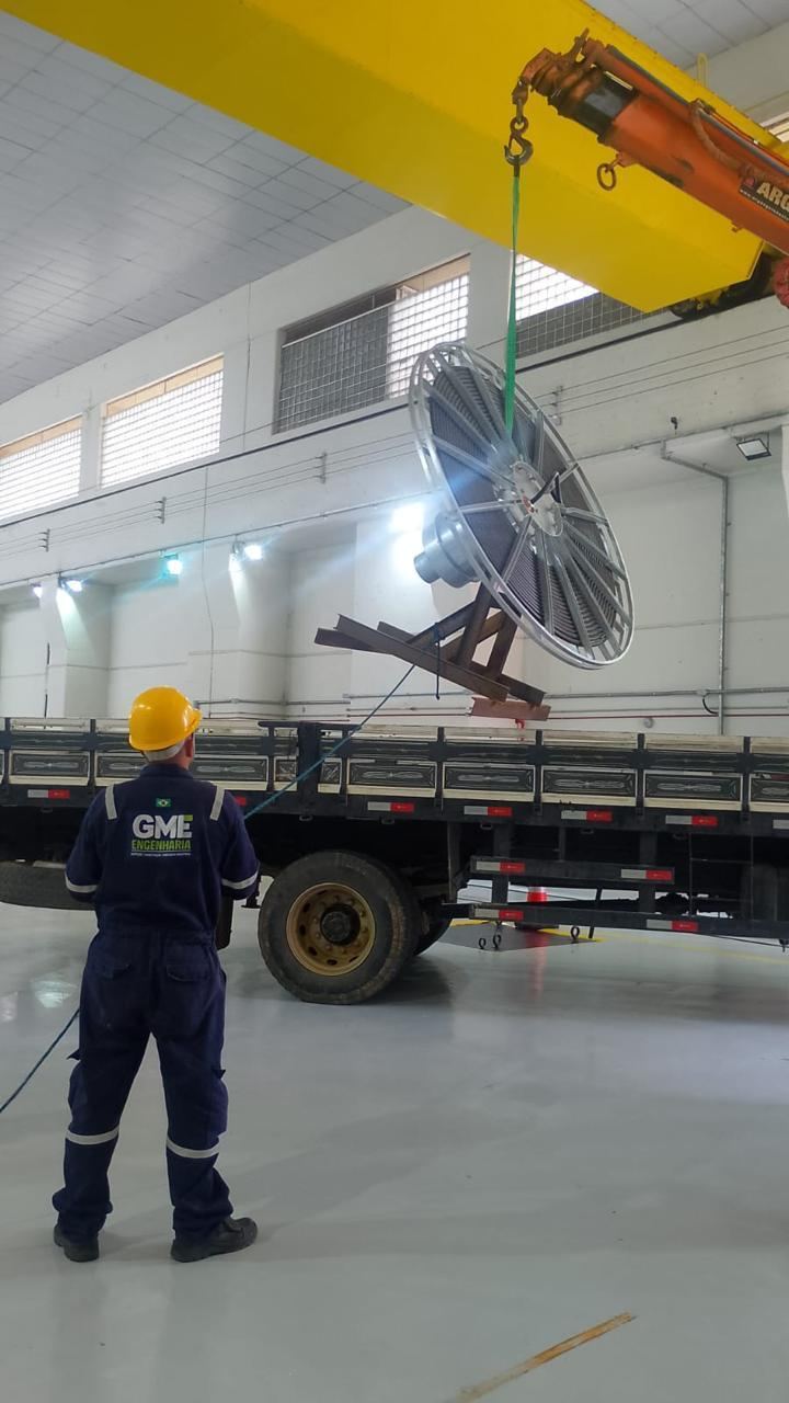 Enrolador de cabos do pórtico principal suspenso por talha dentro de galpão industrial, técnico de costas observando a manobra