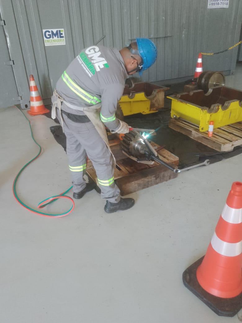 Soldador realizando solda com maçarico em campo, sinalização com cones de segurança ao redor