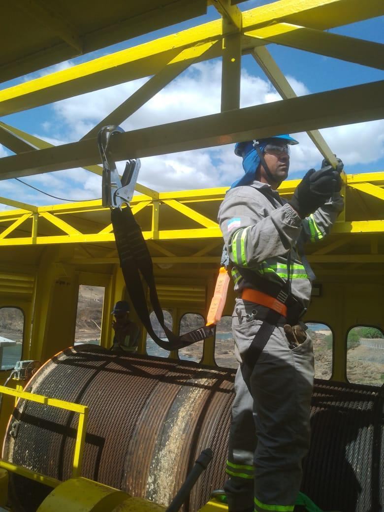 Técnico fixando cabo em treliça metálica amarela, a céu aberto com nuvens ao fundo